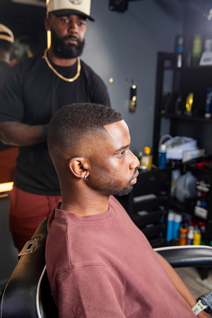Client seated in the barber chair before the cut, barber standing behind him listening