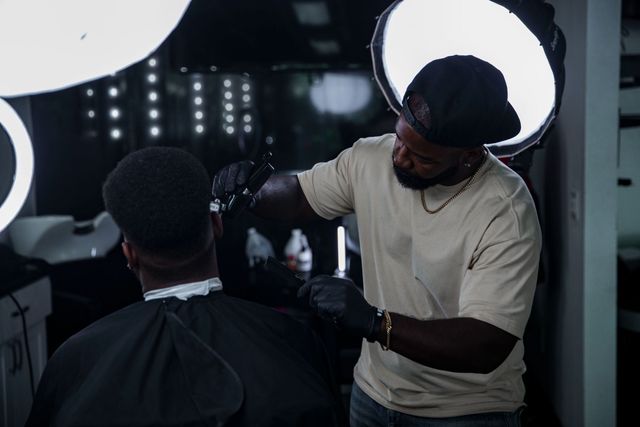 A barber working between glowing ring lights after dark